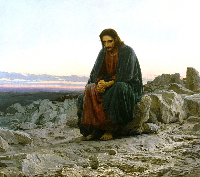 A painting of Jesus in a desolate place. He is sitting on a boulder with his hands together. Rocks are all around Him and there are no trees. He is looking downward like He is deep in thought. This could be Him during His time in the wilderness, or when He left to go pray.