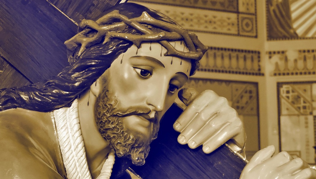 A close-up of a statue of Jesus. He is carrying His cross with a crown of thorns on His head. Drops of blood can be seen on His forehead, and other places of His head.