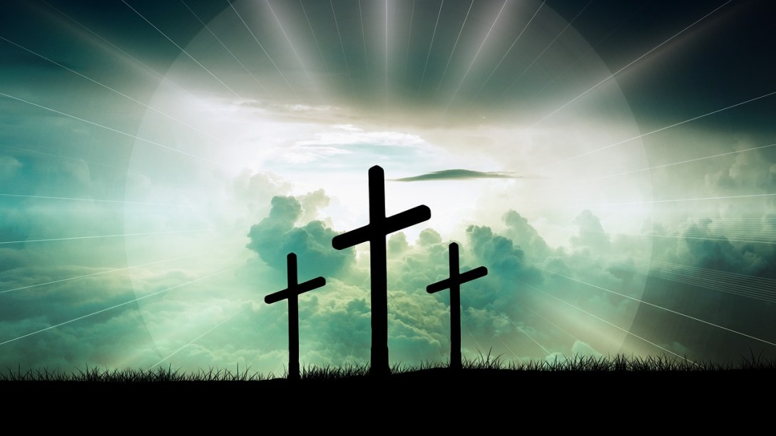 Three crosses are seen the horizon. Behind them light is shining and clouds are visible.