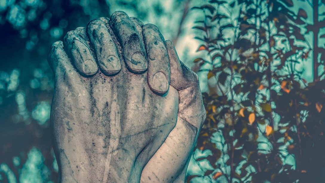 A sculpture of praying hands next to some trees.
