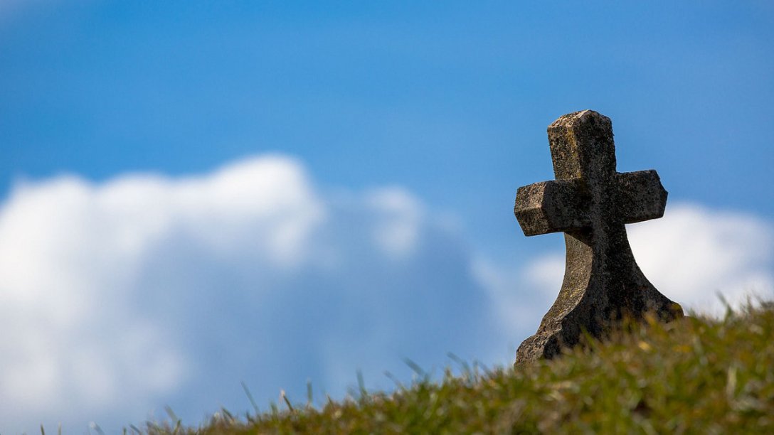 A small cross on a grave with the sky visible in the background.