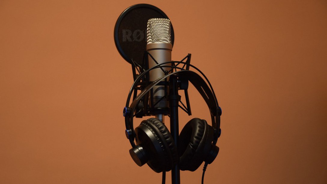 A microphone sitting on its stand, with a pop filter in front of it, and headphones hanging next to it.