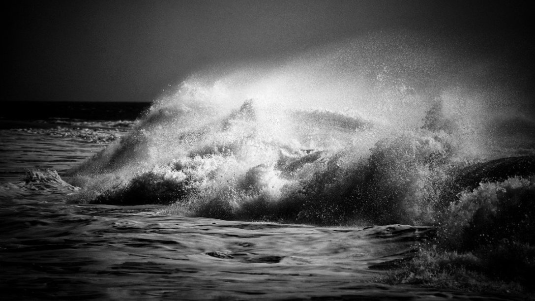 Waves crashing near a seashore with a strong contrast between black and white in the image.