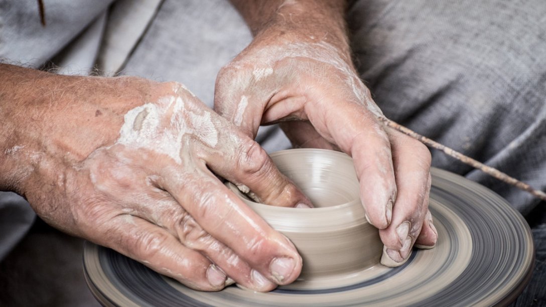 Two hands of a potter working on shaping a cup.